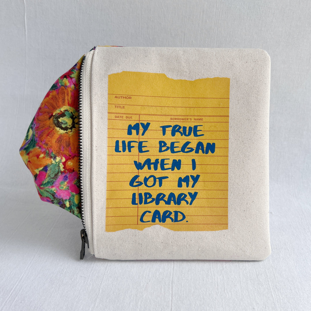 padded canvas zip bag with a yellow  library card and the words, My True Life began when I got a Library Card, plus a colorful zipper pull and lining