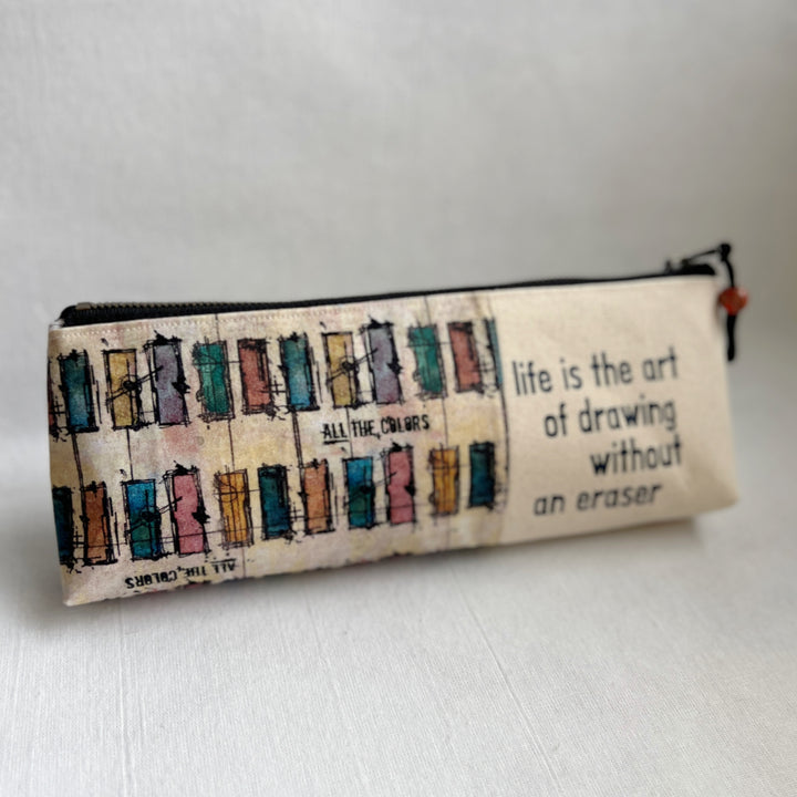 Rectangular zip bag in linen colored canvas and multicolored canvas. Black vinyl lettering decorates one side, with the words, "life is the art of drawing without an eraser." Used for pencil or art tools.