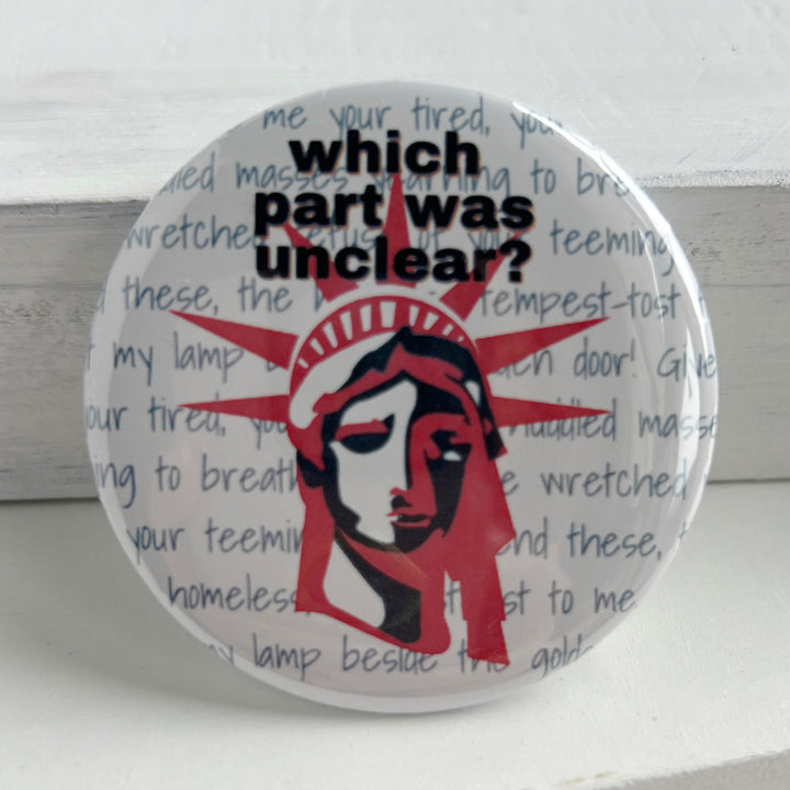 round pinback button with a white background, grey words spelling out some of the words on the base of Lady Liberty, such as give me your poor, your tired, your huddle masses. The words, "which part was unclear " label the top of the button, with a picture of Lady Liberty's head in red and blue.