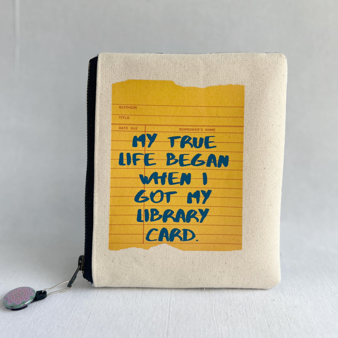 padded canvas zip bag with a yellow  library card and the words, My True Life began when I got a Library Card, plus a colorful zipper pull and lining