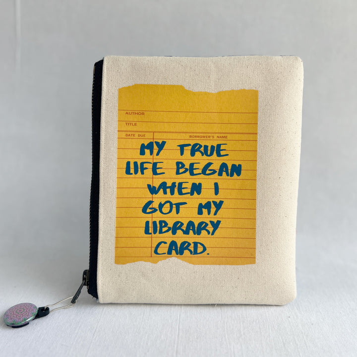 padded canvas zip bag with a yellow  library card and the words, My True Life began when I got a Library Card, plus a colorful zipper pull and lining