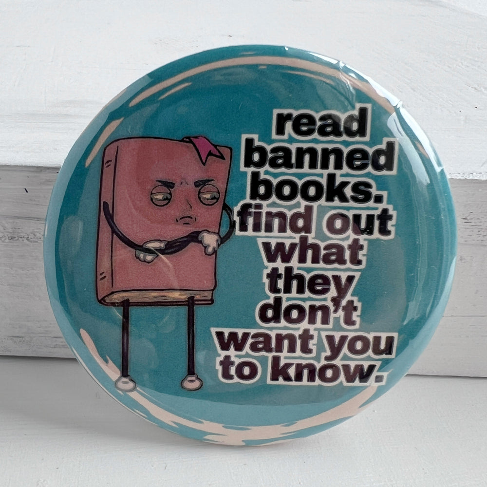 round pinback button with a teal blue background, a cartoon figure of a book with an angry face, and the words, "read banned book. find out what they don't want you to know."