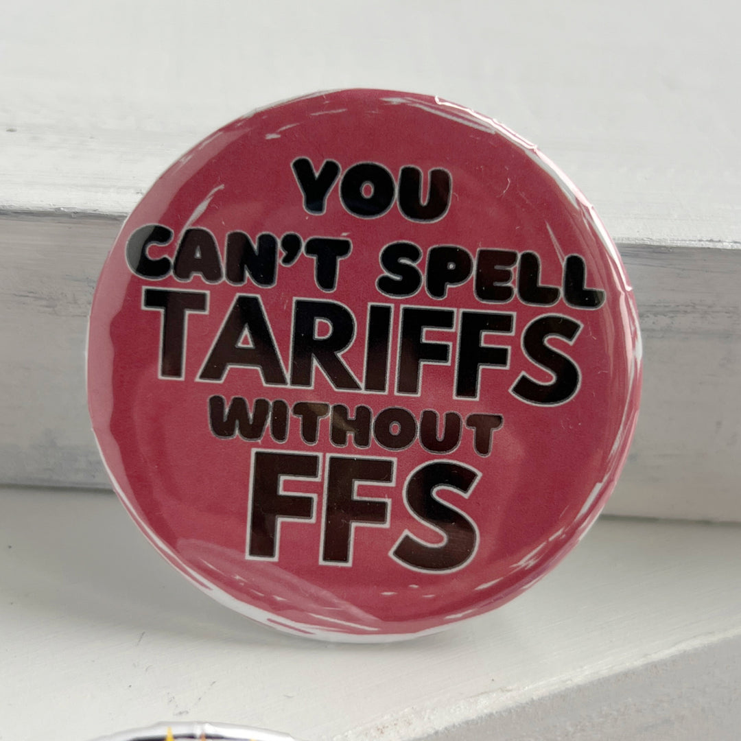 round pinback button with a pink background and the words, "you can't spell TARIFFS without FFS" in black lettering.