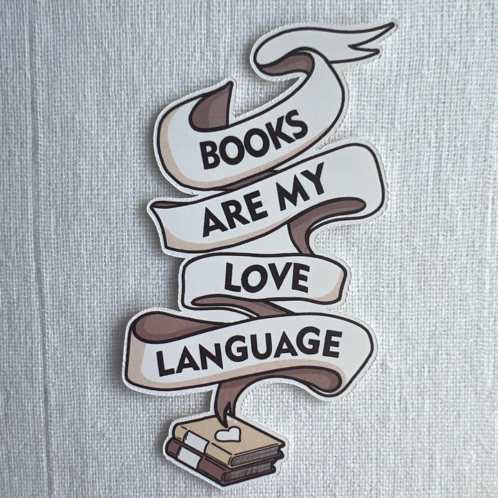 Three inch high sticker consisting of a white ribbon swirling out of a book, with the words, "Books are my love language" in black lettering.