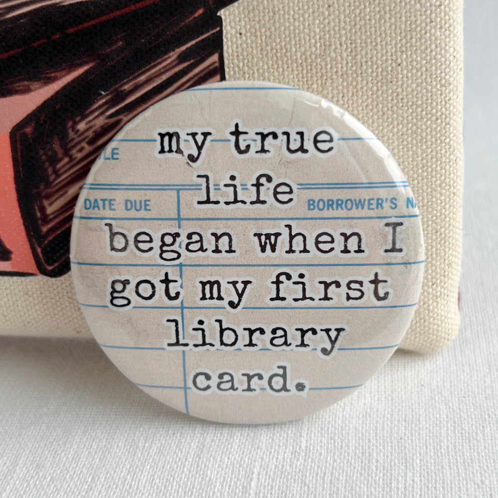 round pinback button with a library checkout card background and the words, "my true life began when I got my first library card."