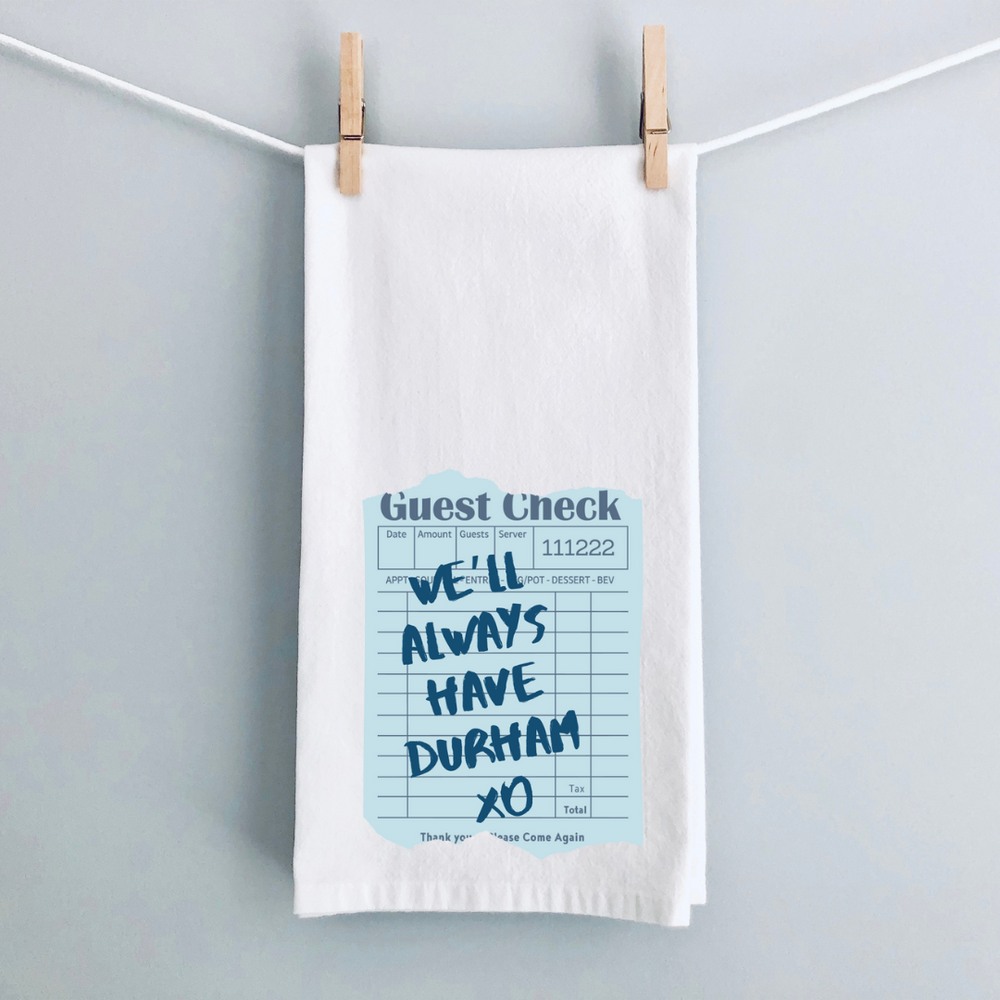 A white kitchen towel with a vintage guest check note in blue and the words, We'll always have Durham xo.