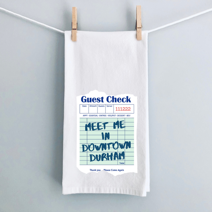 A white kitchen towel with a vintage guest check note in blue and the words, Meet me in downtown Durham