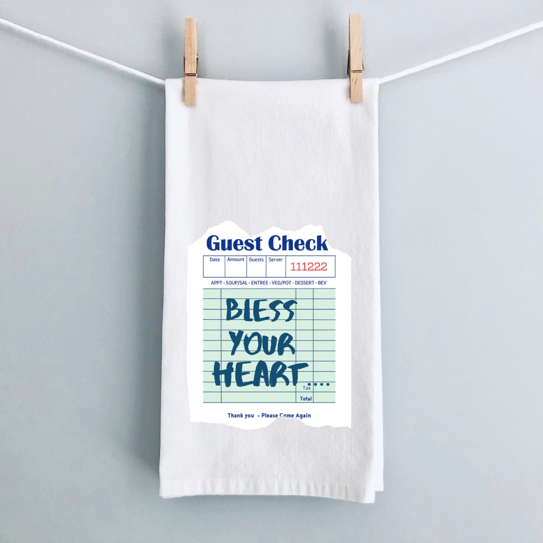 A white kitchen towel with a vintage guest check note in blue and the words, Bless your heart.