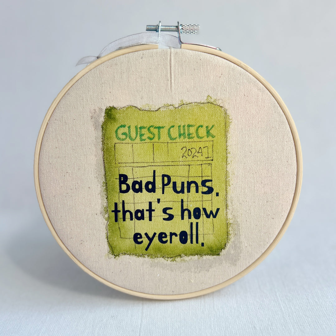 original hoop art piece with a faded guest check ticket painted in citron green with the words, bad puns, that's how eyeroll, in black vinyl lettering