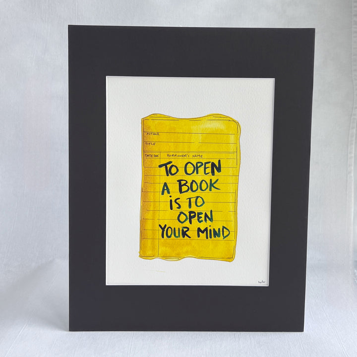 an original watercolor painting depicting a torn vintage library checkout card in shades of yellow with the words, my true life began when I got my library card, matted in black