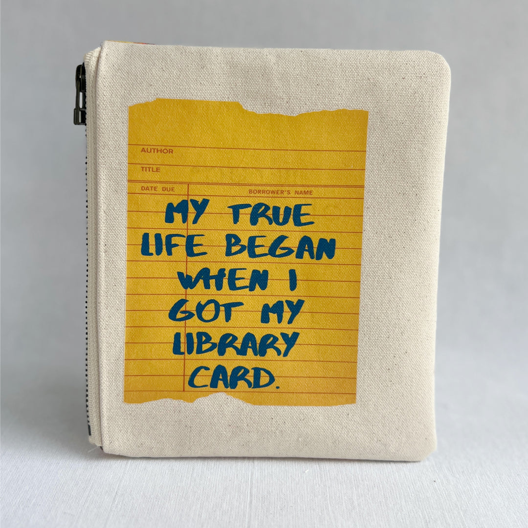 padded canvas zip bag with a yellow  library card and the words, My True Life began when I got a Library Card, plus a colorful zipper pull and lining