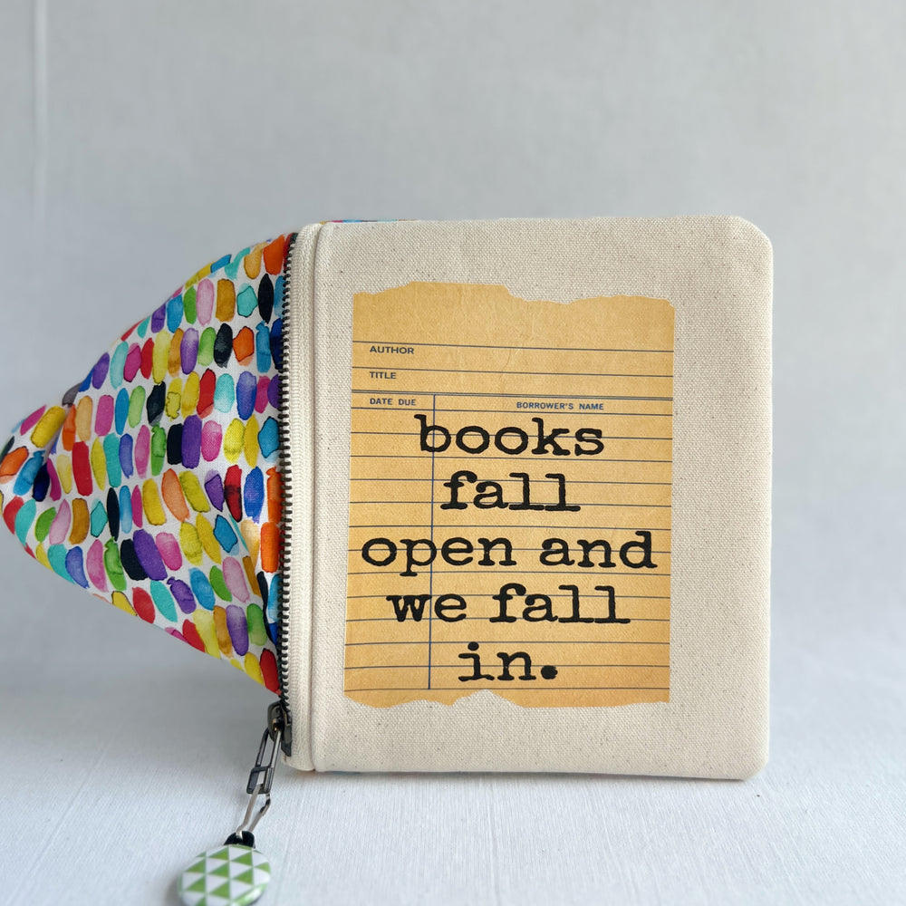 padded canvas zip bag with a yellow  library card and the words, Books fall open and we fall in, plus a colorful zipper pull and lining