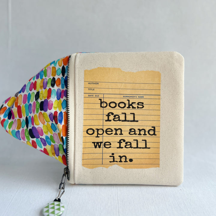 padded canvas zip bag with a yellow  library card and the words, Books fall open and we fall in, plus a colorful zipper pull and lining