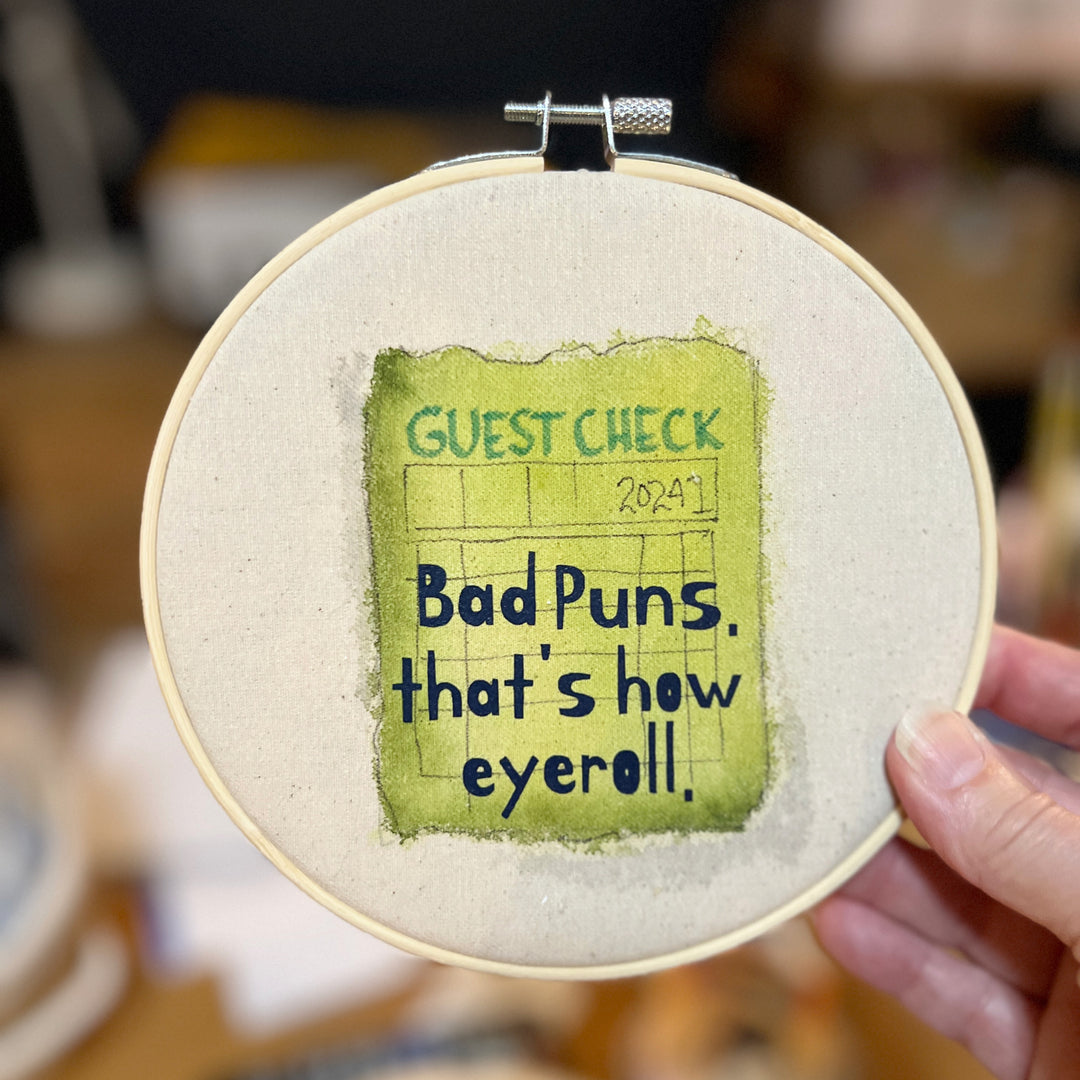 original hoop art piece with a faded guest check ticket painted in citron green with the words, bad puns, that's how eyeroll, in black vinyl lettering