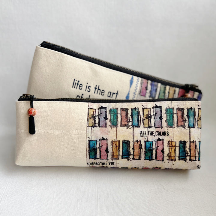 Rectangular zip bag in linen colored canvas and multicolored canvas. Black vinyl lettering decorates one side, with the words, "life is the art of drawing without an eraser." Used for pencil or art tools.