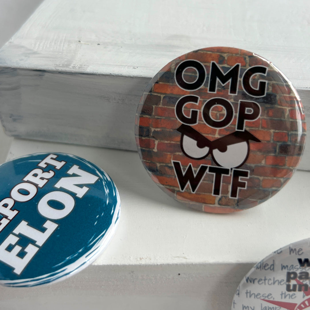 round pinback button with a blue background and the words, "Deport Elon" in white. A second round pinback button has a red brick background, with the letters, OMG GOP WTF and an angry face.