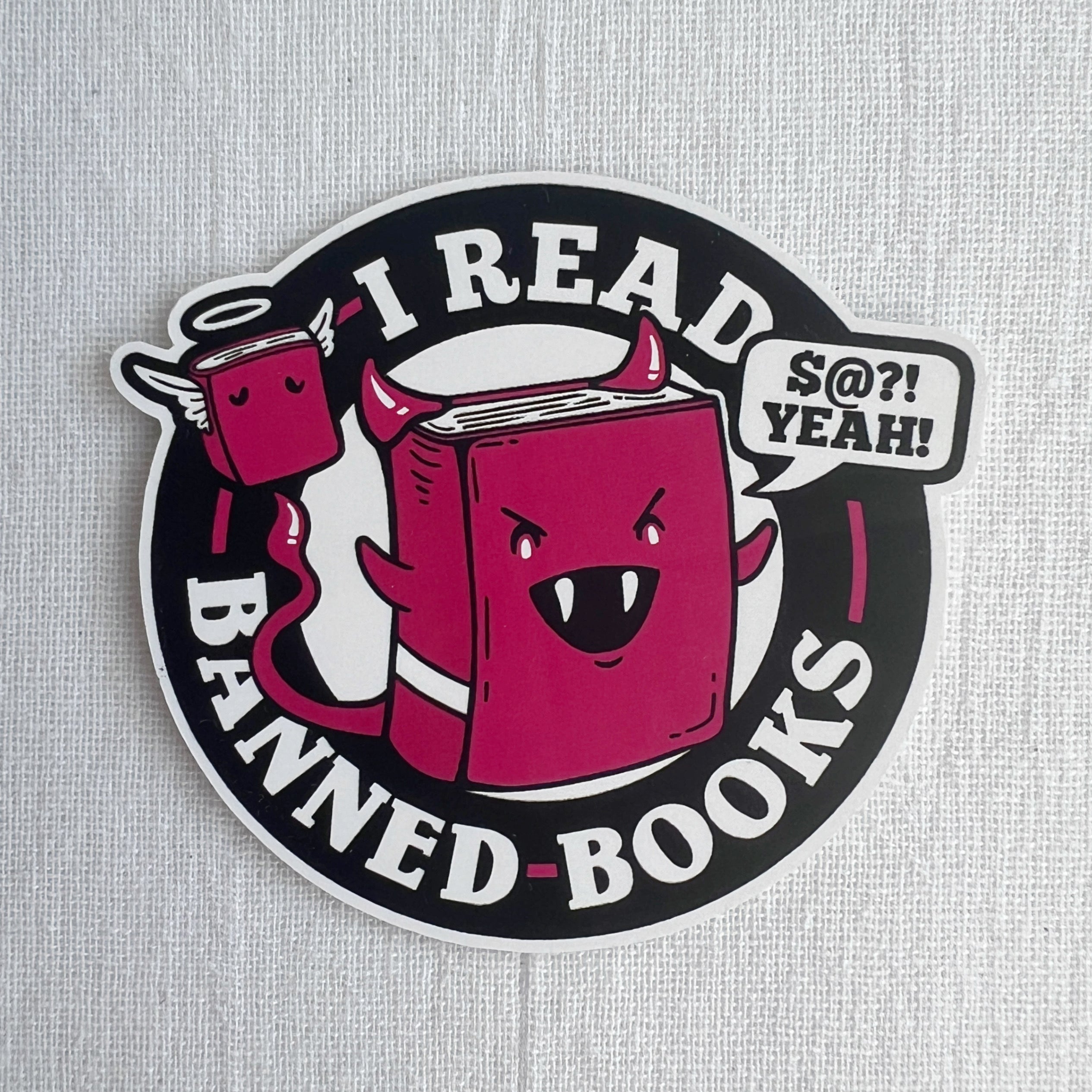 Round three inch sticker with black and white background. Red cartoon characters include a book with horns and a book with wings.  Wording is I read banned books, with a word bubble containing S@?! yeah!