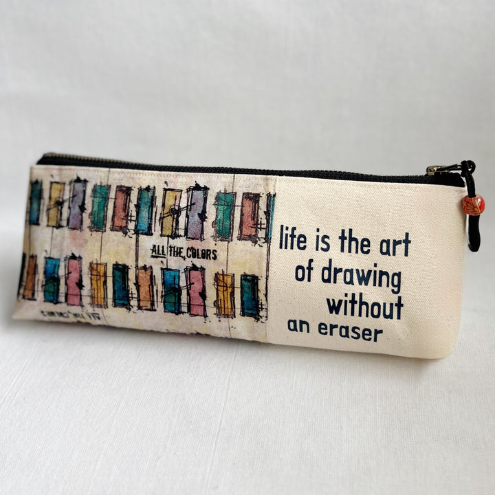 Rectangular zip bag in linen colored canvas and multicolored canvas. Black vinyl lettering decorates one side, with the words, "life is the art of drawing without an eraser." Used for pencil or art tools.