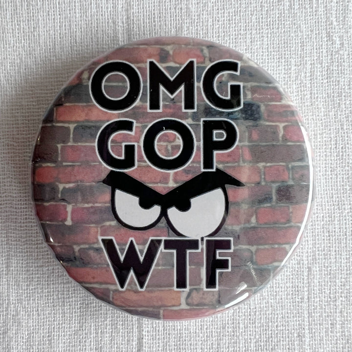 A round pin back button with a red brick background, with the letters, OMG GOP WTF and an angry face.