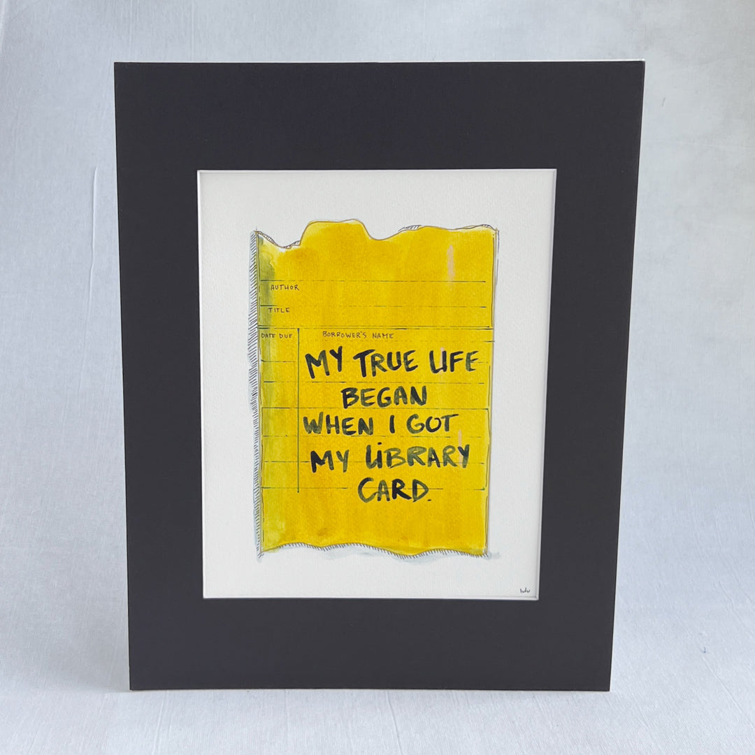 an original watercolor painting depicting a torn vintage library checkout card in shades of yellow with the words, my true life began when I got my library card, matted in black