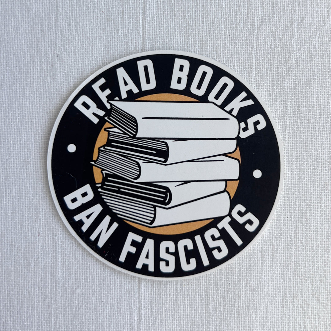 3 inch round sticker with a black background and white lettering reading, Read Books, Ban Fascists.  There is also a black and white graphic design of a 5-book stack.