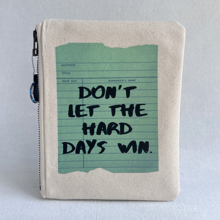 padded canvas zip bag with a green library card and the words, Don't Let the Hard Days Win, plus a colorful zipper pull and lining