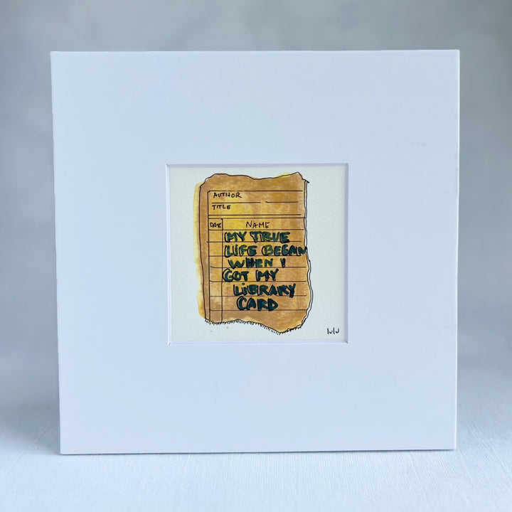 an original watercolor painting depicting a torn vintage library checkout card in shades of yellow with the words, my true life began when I got my library card, matted in white