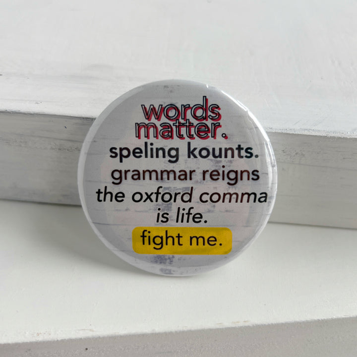 a round pin back button with a white background and the words, "words matter. speling kounts. grammar reins. the oxford comma is life. fight me."