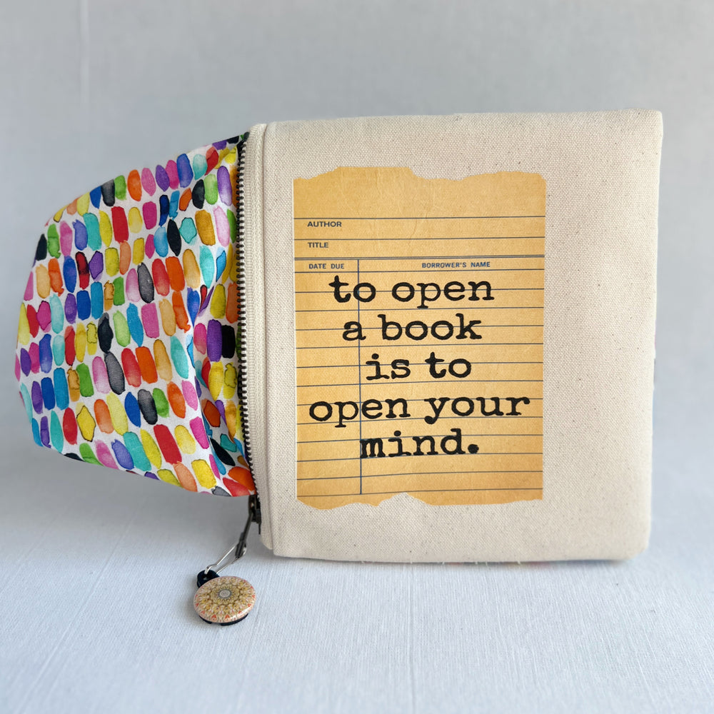 padded canvas zip bag with a yellow  library card and the words, To open a book is to open your mind, plus a colorful zipper pull and lining