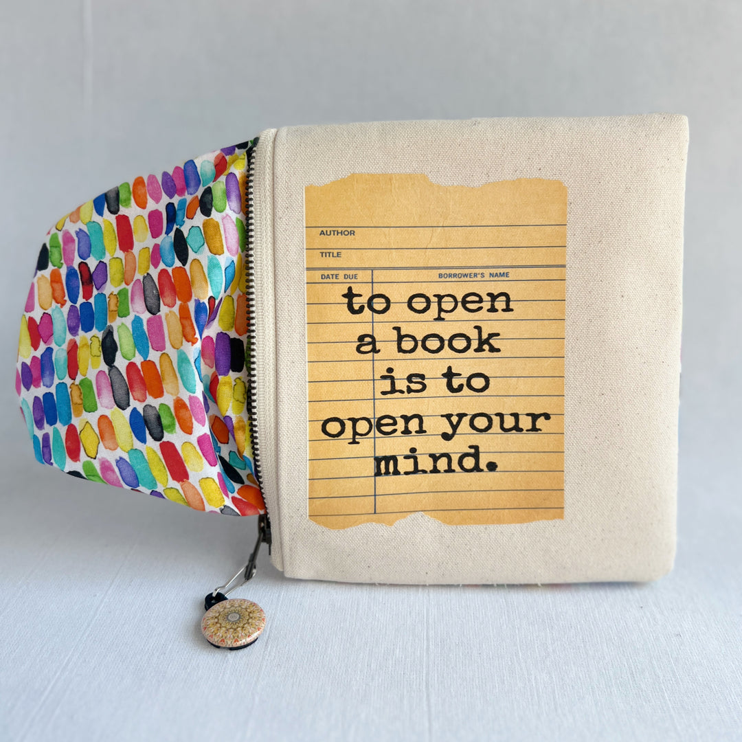 padded canvas zip bag with a yellow  library card and the words, To open a book is to open your mind, plus a colorful zipper pull and lining