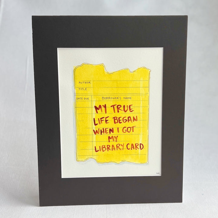 an original watercolor painting depicting a torn vintage library checkout card in shades of yellow with the words, my true life began when I got my library card, matted in black