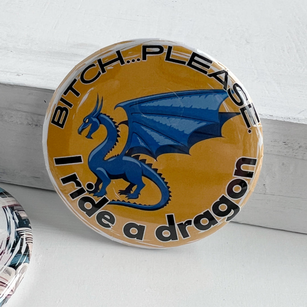 round pinback button with a yellow background, a blue dragon and the words, "bitch..please. I ride a dragon" in black lettering.