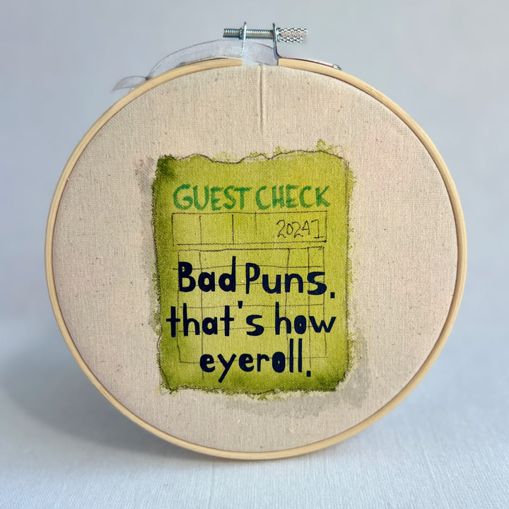 original hoop art piece with a faded guest check ticket painted in citron green with the words, bad puns, that's how eyeroll, in black vinyl lettering