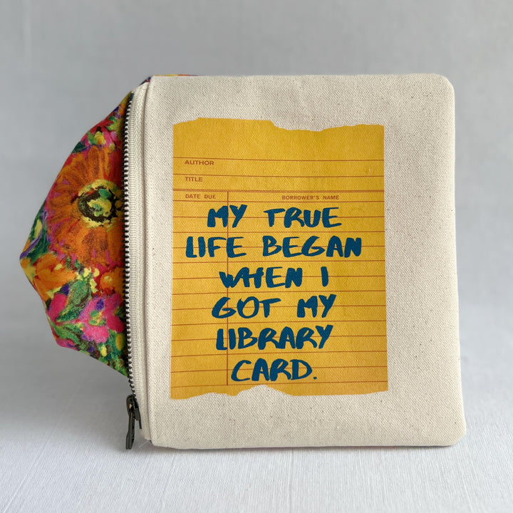 padded canvas zip bag with a yellow  library card and the words, My True Life began when I got a Library Card, plus a colorful zipper pull and lining