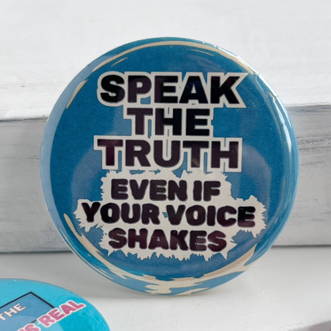 round, blue pinback button on a white background with the words, "speak the truth, even if your voice shakes."