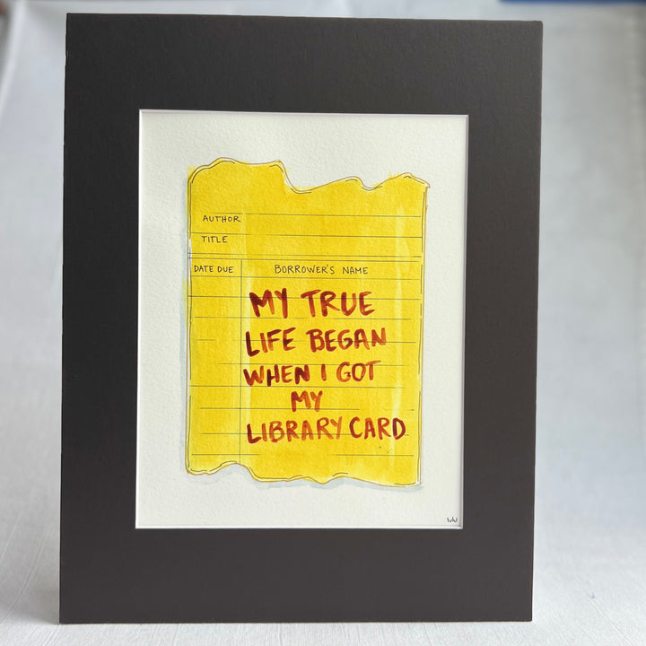 an original watercolor painting depicting a torn vintage library checkout card in shades of yellow with the words, my true life began when I got my library card, matted in black