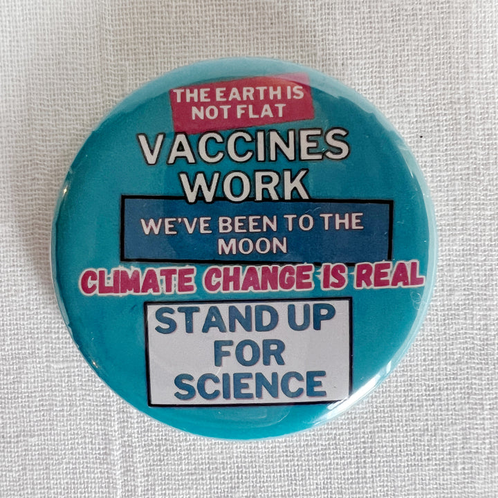 round, robin's egg blue pinback button on a white background with the words, "the earth is not flat. vaccines work. we've been to the moon. climate change is real. stand up for science."