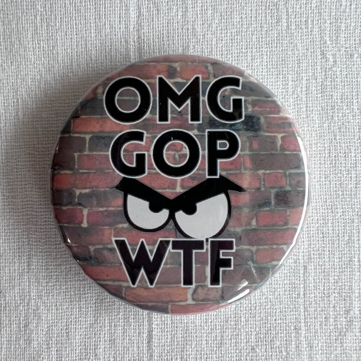 A round pin back button with a red brick background, with the letters, OMG GOP WTF and an angry face.